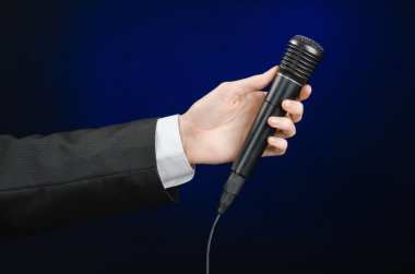 Business speech and topic: a man in a black suit holding a black microphone on a dark blue background in studio isolated