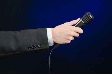 Business speech and topic: a man in a black suit holding a black microphone on a dark blue background in studio isolated