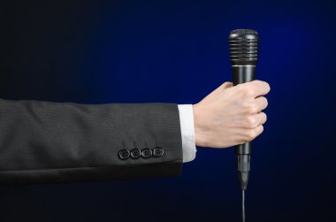 Business speech and topic: a man in a black suit holding a black microphone on a dark blue background in studio isolated
