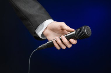 Business speech and topic: a man in a black suit holding a black microphone on a dark blue background in studio isolated
