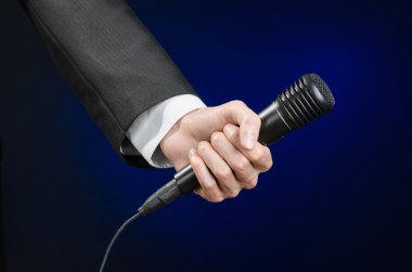 Business speech and topic: a man in a black suit holding a black microphone on a dark blue background in studio isolated