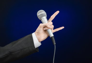 Business and speech topic: Man in black suit holding a microphone on a gray dark blue isolated background in studio