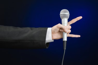 Business and speech topic: Man in black suit holding a microphone on a gray dark blue isolated background in studio