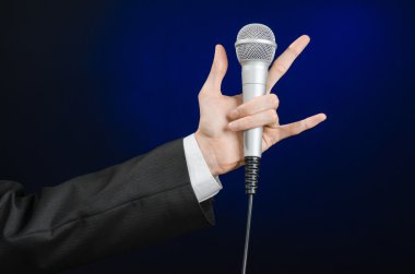 Business and speech topic: Man in black suit holding a microphone on a gray dark blue isolated background in studio