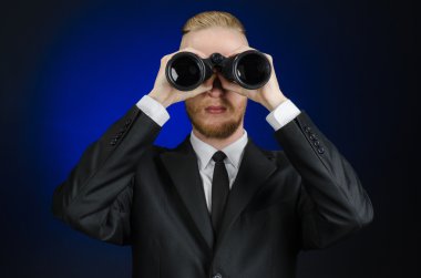 Business and search topic: Man in black suit holding a black binoculars in hand on a dark blue background in studio isolated clipart