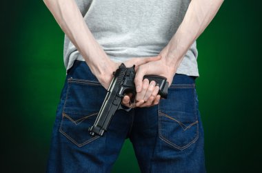 Firearms and murderer topic: man in a gray t-shirt holding a gun on a dark green background isolated in studio