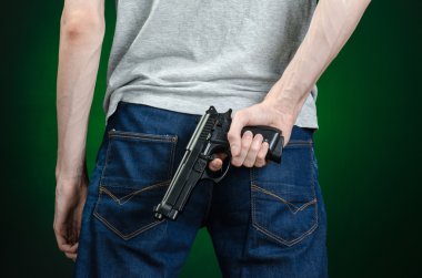 Firearms and murderer topic: man in a gray t-shirt holding a gun on a dark green background isolated in studio