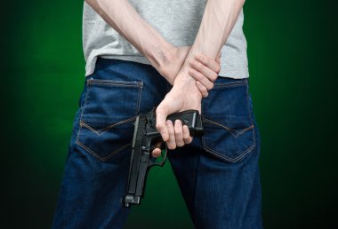 Firearms and murderer topic: man in a gray t-shirt holding a gun on a dark green background isolated in studio