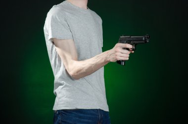Firearms and murderer topic: man in a gray t-shirt holding a gun on a dark green background isolated in studio