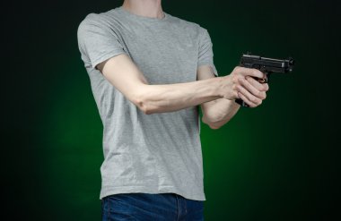 Firearms and murderer topic: man in a gray t-shirt holding a gun on a dark green background isolated in studio