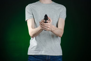 Firearms and murderer topic: man in a gray t-shirt holding a gun on a dark green background isolated in studio