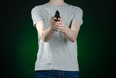 Firearms and murderer topic: man in a gray t-shirt holding a gun on a dark green background isolated in studio