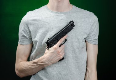 Firearms and murderer topic: man in a gray t-shirt holding a gun on a dark green background isolated in studio