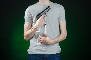 Firearms and murderer topic: man in a gray t-shirt holding a gun on a dark green background isolated in studio
