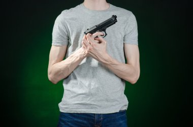 Firearms and murderer topic: man in a gray t-shirt holding a gun on a dark green background isolated in studio