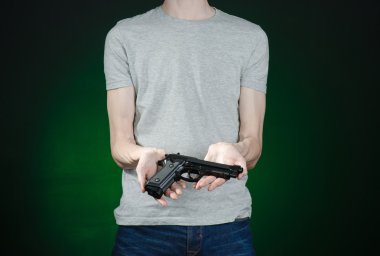 Firearms and murderer topic: man in a gray t-shirt holding a gun on a dark green background isolated in studio