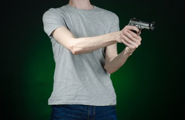 Firearms and murderer topic: man in a gray t-shirt holding a gun on a dark green background isolated in studio