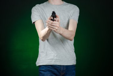 Firearms and murderer topic: man in a gray t-shirt holding a gun on a dark green background isolated in studio