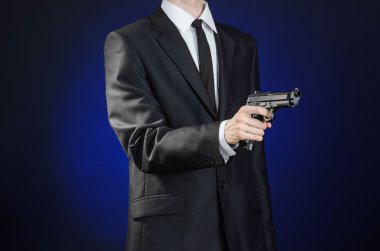 Firearms and security topic: a man in a black suit holding a gun on a dark blue background in studio isolated