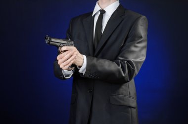 Firearms and security topic: a man in a black suit holding a gun on a dark blue background in studio isolated