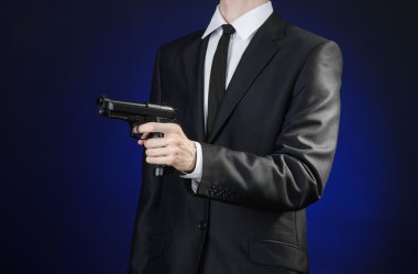 Firearms and security topic: a man in a black suit holding a gun on a dark blue background in studio isolated