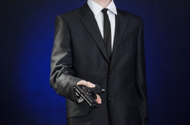Firearms and security topic: a man in a black suit holding a gun on a dark blue background in studio isolated