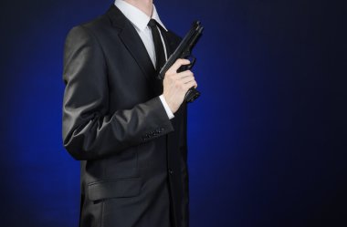 Firearms and security topic: a man in a black suit holding a gun on a dark blue background in studio isolated