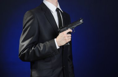 Firearms and security topic: a man in a black suit holding a gun on a dark blue background in studio isolated