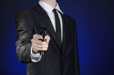 Firearms and security topic: a man in a black suit holding a gun on a dark blue background in studio isolated