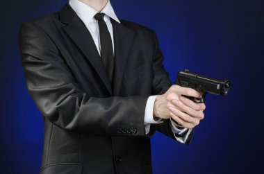 Firearms and security topic: a man in a black suit holding a gun on a dark blue background in studio isolated