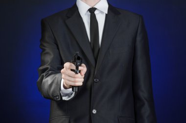 Firearms and security topic: a man in a black suit holding a gun on a dark blue background in studio isolated