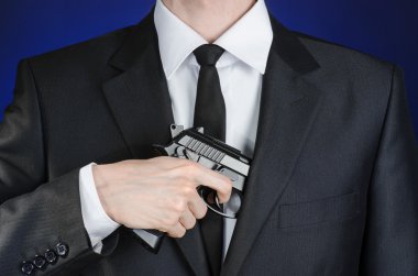 Firearms and security topic: a man in a black suit holding a gun on a dark blue background in studio isolated