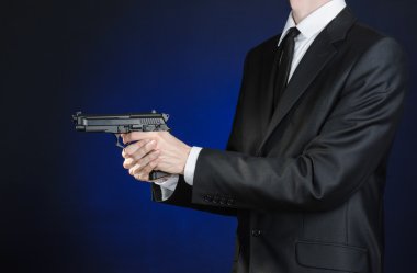 Firearms and security topic: a man in a black suit holding a gun on a dark blue background in studio isolated