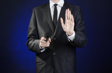 Firearms and security topic: a man in a black suit holding a gun on a dark blue background in studio isolated