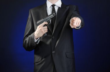 Firearms and security topic: a man in a black suit holding a gun on a dark blue background in studio isolated