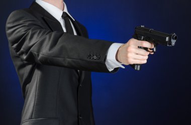 Firearms and security topic: a man in a black suit holding a gun on a dark blue background in studio isolated