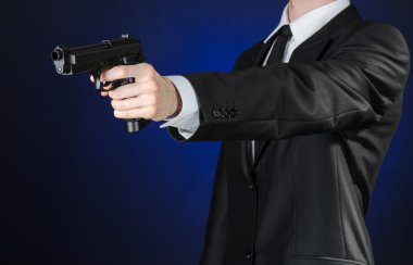 Firearms and security topic: a man in a black suit holding a gun on a dark blue background in studio isolated