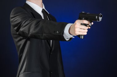 Firearms and security topic: a man in a black suit holding a gun on a dark blue background in studio isolated