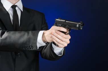 Firearms and security topic: a man in a black suit holding a gun on a dark blue background in studio isolated