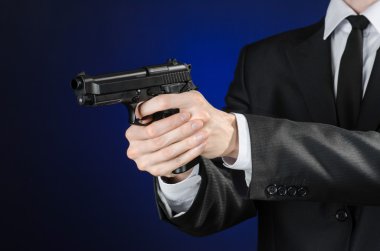 Firearms and security topic: a man in a black suit holding a gun on a dark blue background in studio isolated