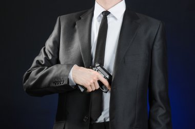 Firearms and security topic: a man in a black suit holding a gun on a dark blue background in studio isolated