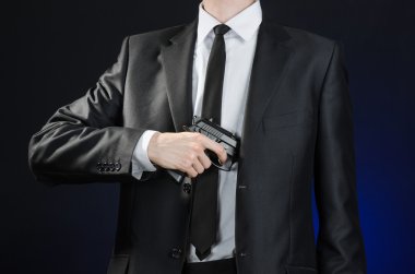 Firearms and security topic: a man in a black suit holding a gun on a dark blue background in studio isolated