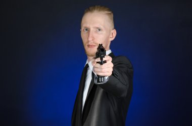 Firearms and security topic: a man in a black suit holding a gun on a dark blue background in studio isolated
