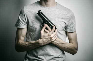 Horror and firearms topic: suicide with a gun on a gray background in the studio