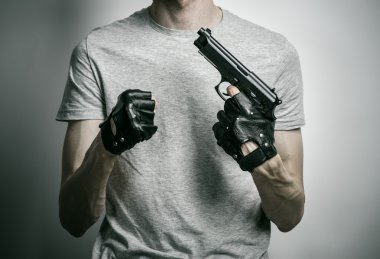 Horror and firearms topic: the killer with a gun in his hand in black gloves on a gray background in the studio
