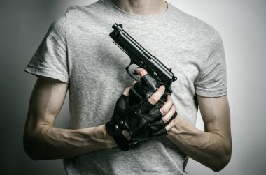 Horror and firearms topic: the killer with a gun in his hand in black gloves on a gray background in the studio