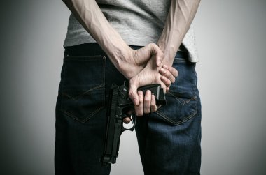 Horror and firearms topic: crazed killer with a gun on a gray background in the studio
