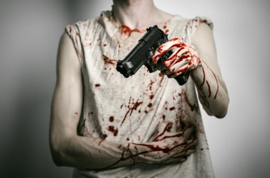 Horror and firearms topic: the bloody killer with a gun on a gray background in the studio