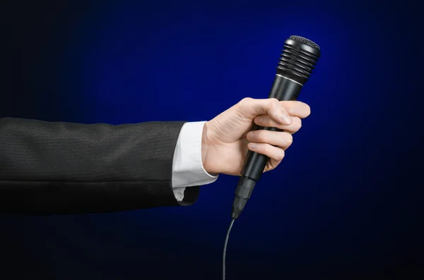 Business speech and topic: a man in a black suit holding a black microphone on a dark blue background in studio isolated — Stockfoto