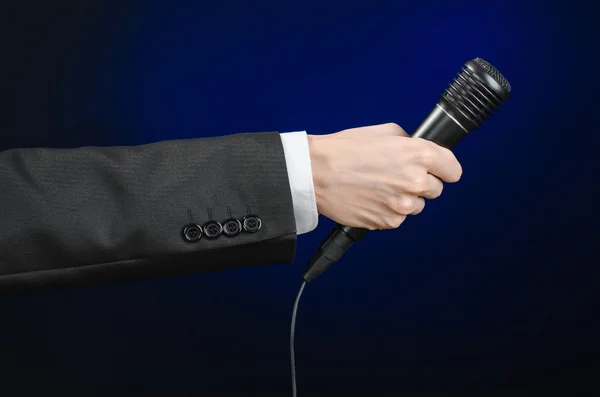 Business speech and topic: a man in a black suit holding a black microphone on a dark blue background in studio isolated — 스톡 사진